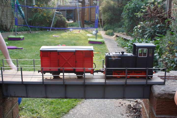 Black diesel loco crossing a steel bridge with a red van