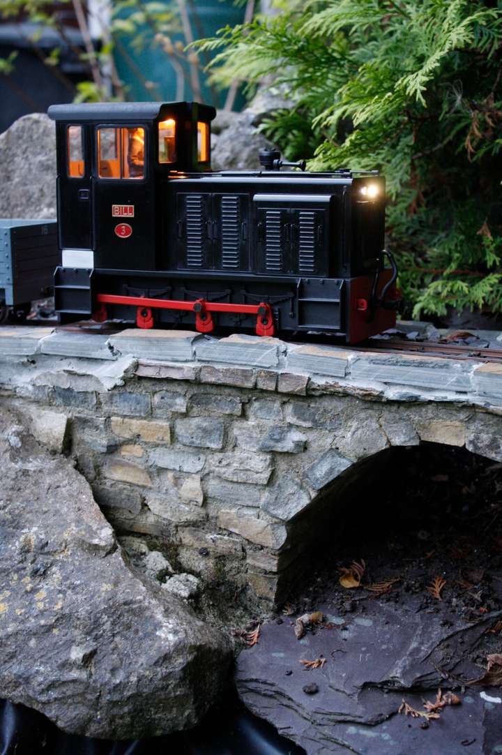 Black diesel loco crossing a stone bridge at dusk, with the cab lights on