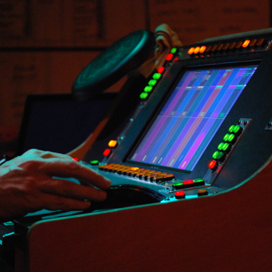 Hands operating a lighting console with glowing buttons