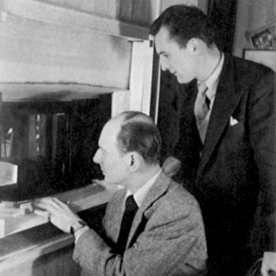 Black and white picture of two men looking into a model of a theatre stage