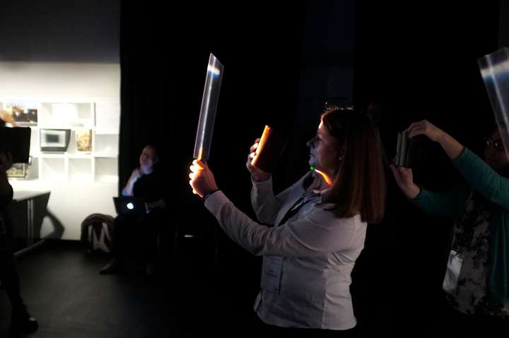 Darkened room with people holding up small perspex screens in narrow cuts of light