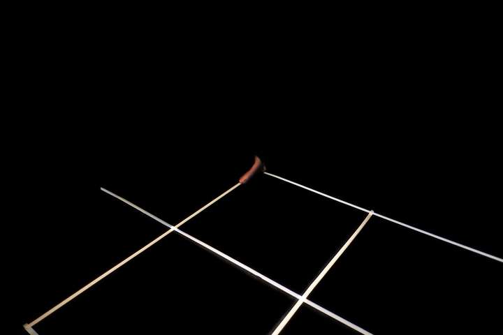 Grid of white lines in a dark space. Parts of the performer's body are glimpsed in narroew cuts of light