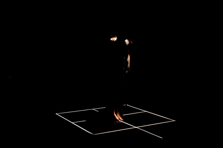 Grid of white lines in a dark space. Parts of the performer's body are glimpsed in narroew cuts of light