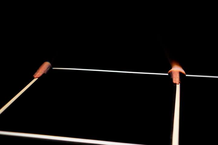Grid of white lines in a dark space. Parts of the performer's body are glimpsed in narroew cuts of light